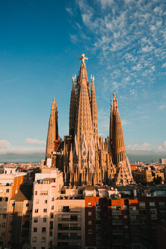 Rooftop view of the Sagrada Familia basilica towers at sunset with the central Jesus Christ tower and cross under a blue sky.
