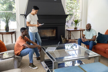 Naklejka premium Diverse male friends leaning and discussing in living room around glass coffee table with laptop