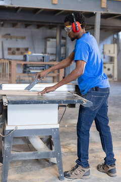 Table saw cutting long wood board in carpentry workshop, with dust collection hose attached