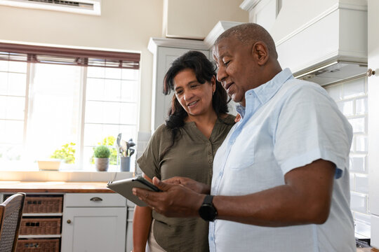 Mature couple standing side-by-side viewing tablet in bright kitchen with plants