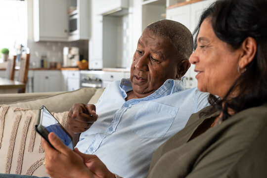 African American couple sitting on sofa in living room, man pointing at phone, woman holding phone