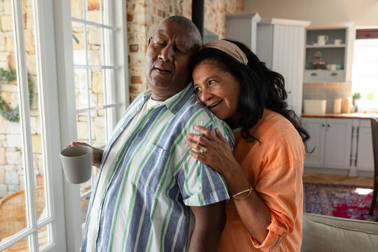 Senior African American couple standing at home near doors, man holding mug, woman in orange blouse