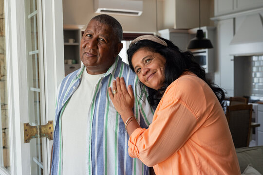 African American senior couple standing at glass door, leaning together, showing ring and bracelet