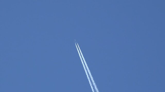 Low angle view of distant commercial jet aircraft cruising at high altitude with two parallel white contrails across deep clear blue sky with copy space