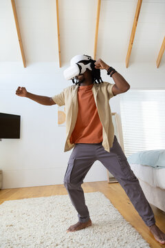 African American man standing in loft bedroom wearing white VR headset and interacting with VR