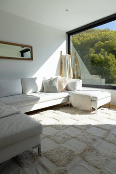 White sectional sofa with chaise lounge is bathing in sunlight at black-framed window, soft throws