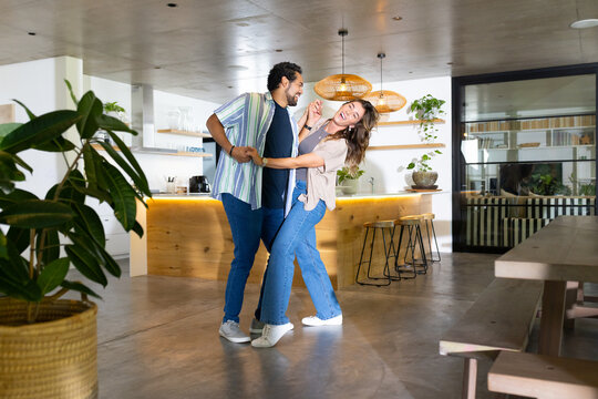 Couple dancing near wooden kitchen island under rattan pendant lamps with plants and bar stools