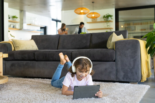 African American family watching child lying on shag rug using tablet and headphones in living room