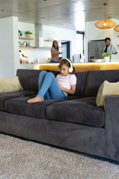 Family relaxing in modern open-plan living room, child wearing white headphones using tablet