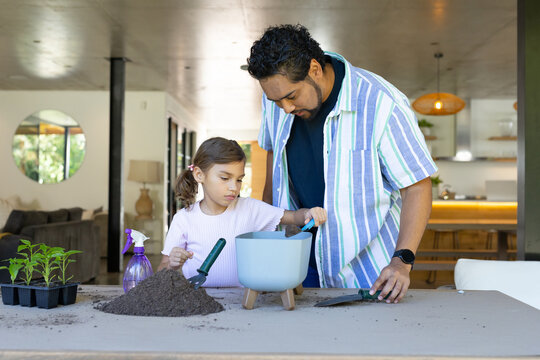 African American father guiding child, potting plants at home with raised planter, soil, trowels