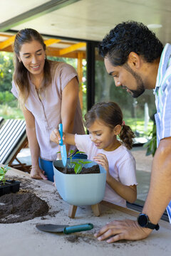 Diverse family with child planting seedling at covered patio using blue planter and blue trowel
