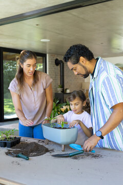 Parents with child potting seedlings at covered patio table with planter, soil, blue trowel
