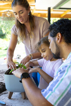 Diverse family planting small green seedling in raised planter on covered patio with blue trowel