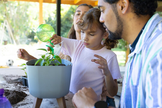 African American family guiding child girl pouring water into planter on porch with green can