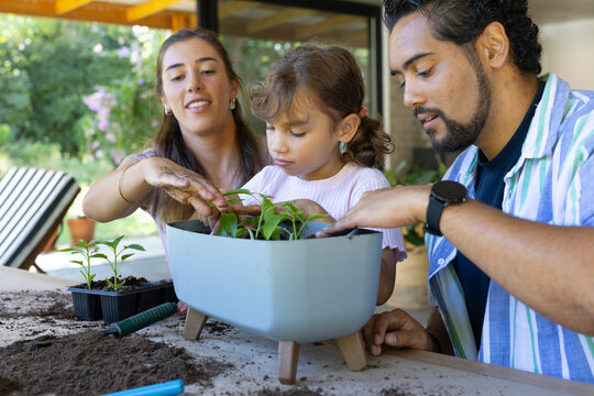 Family guiding child planting seedlings on covered patio using pale blue planter and trowel