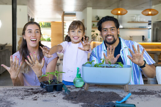 Family holding up soil-covered palms at table in modern kitchen, showing planter and seedling tray