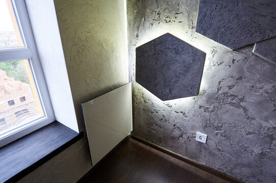 Decorative textured wall with illuminated hexagon panel and electric radiator beside window, close up view of modern interior corner. Home decor, ambient lighting and renovation concept.
