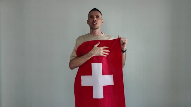 A patriotic man proudly sings the Swiss national anthem while holding the Swiss flag. An emotional sports fan cheers on his favorite team