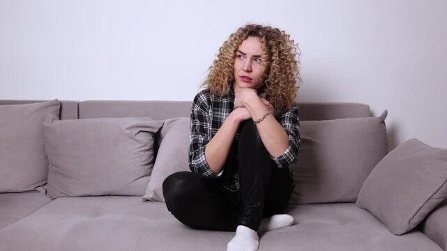Person sitting on a couch with tense posture and upward gaze, creating a subtle atmosphere of fear, suspense and mild paranoia in a simple home interior.