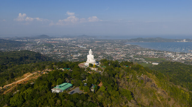 Aerial view of the Great Buddha of Phuket on a lush hilltop overlooking the coastal city and bay under a clear blue sky Tambon Karon, Chang Wat Phuket, Thailand.