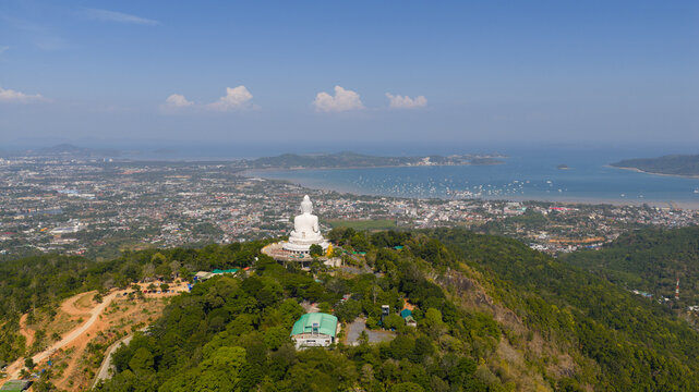 Aerial view of the Big Buddha statue on a lush green hilltop overlooking the coastal town and bay with boats in Tambon Karon, Chang Wat Phuket, Thailand.