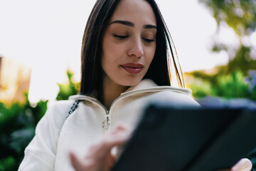 Close up of focused woman using digital tablet application in urban park setting. Female user browsing internet or working on mobile device, connectivity and modern technology concept. © BullRun