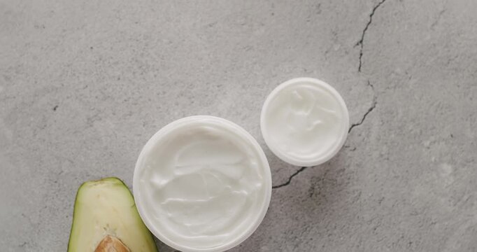 White Jars and tubes with avocado for cosmetics rotate on a gray concrete background in studio. Cosmetics oils based on natural ingredients, scrub, body care. Group of different cosmetic bottles.