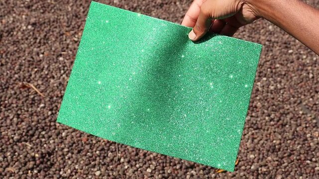 Glitter paper green in color glittering when exposed to sunlight on the outdoors. Shining green paper sheet with light sparkles