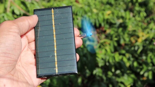 Solar panel when exposed to sunlight is powering a coreless motor with plastic propeller spinning held in the hand