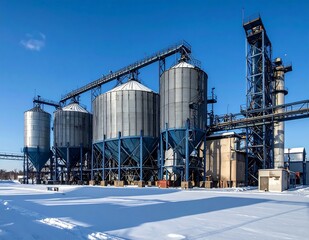 Obraz premium Industrial Grain Silo Storage Facility With Blue Metal Tanks And Conveyor Systems Standing On Snowy Ground Under Clear