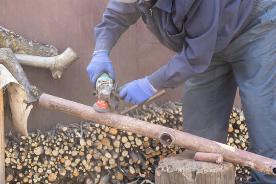 Industrial worker uses an electric angle grinder to smooth and cut a rusty metal pipe, demonstrating metalworking precision and professional construction site maintenance task implementation