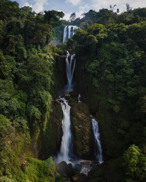 Aerial view of Curug Sewu Waterfall cascading through dense tropical jungle and lush green vegetation in Kecamatan Patean, Central Java, Indonesia.