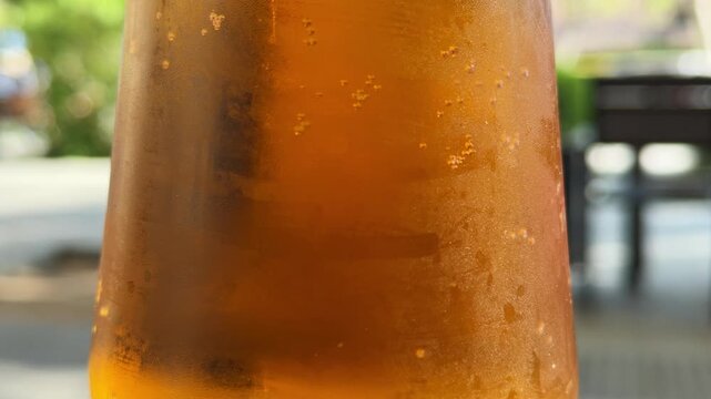 Cold fresh draft beer in frosty glass with bubbles and condensation drops, refreshing amber lager close up on outdoor cafe terrace, summer alcoholic beverage at bar, blurred green background macro