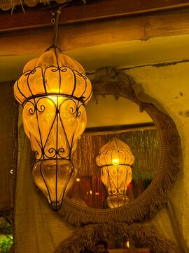 A vintage hanging lamp with a warm glow, surrounded by a decorative mirror. The setting has a cozy, rustic ambiance, ideal for interior design themes.