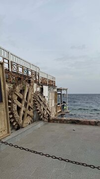 A weathered wooden structure stands near the ocean. The scene features a calm sea and a cloudy sky, creating a serene coastal atmosphere.