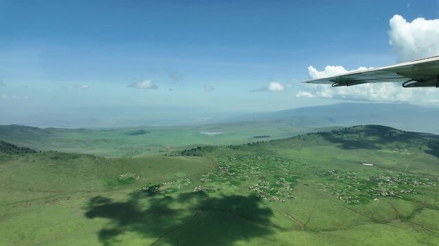 aerial flight over the green maasai region with hills, valleys and villages, wing in view