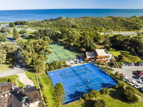 Aerial view of North Shore Community Hub Cafe with people playing on blue and green tennis courts near coastal dunes and the ocean in Kallaroo, Western Australia, Australia.