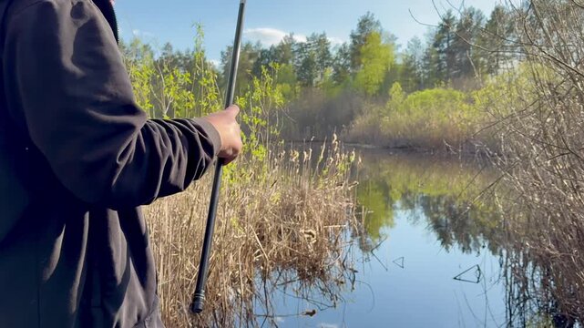 A fisherman casting a float fishing rod into the water from the shore. The rod bends as he throws the line. The float lands on the water surface