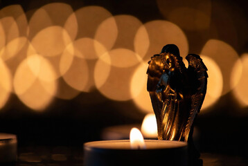 Naklejka premium A bronze angel statue rests on a surface with blurred candlelight, creating a warm and serene atmosphere.