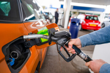Person fuels a car at a gas station in a busy city during midday with other vehicles nearby © Iryna