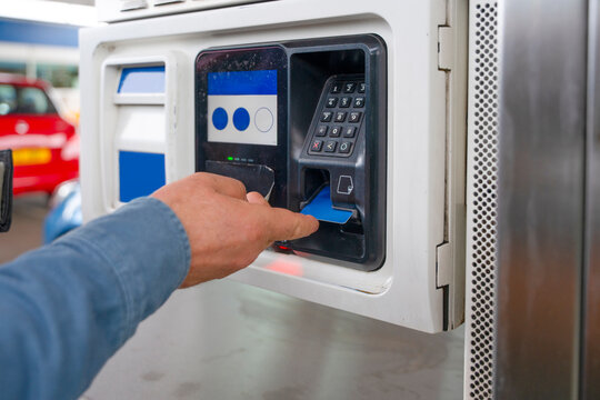 Man pays for fuel at a gas station using a credit card during daylight hours in a busy urban area