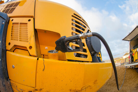 Construction equipment is being refueled at a work site during the day under a clear blue sky