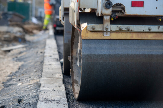 Road construction work seen from the ground with a roller compacting asphalt near a construction site in the day