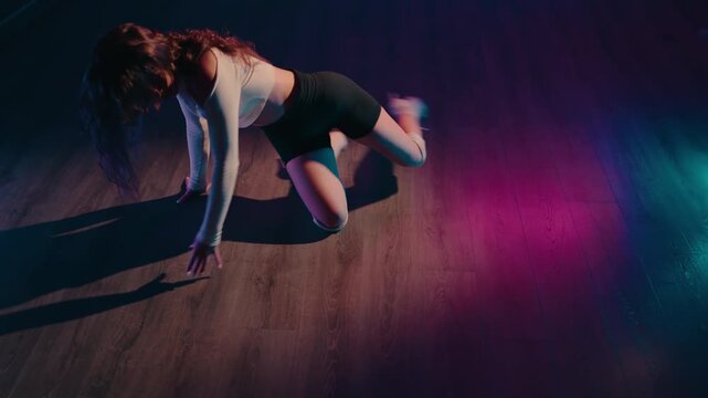 A young woman dances sensually on the floor in high heels and shorts. She moves rhythmically with the music under colorful neon lights. This creates an energetic and captivating atmosphere.
