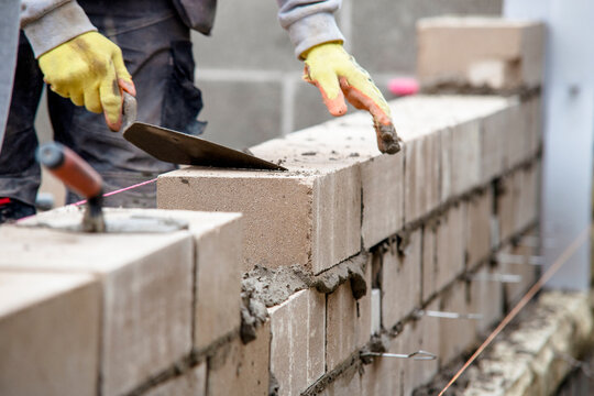 Construction worker lays concrete blocks in a new building site during daylight hours in a residential area