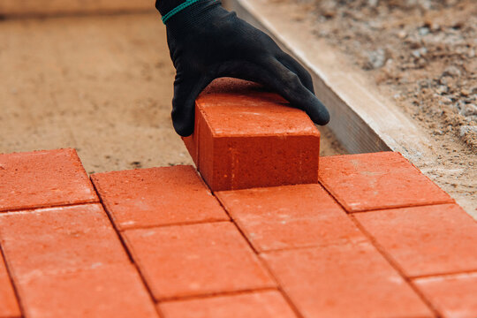 Building a brick pathway with red bricks at a construction site in broad daylight