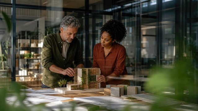 Architects Examining Sustainable Building Model with Greenery in Modern Design Studio Workspace