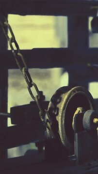 A chain connects to a pulley that is part of a mechanical system at a construction site. It is daytime and the machinery is in use for lifting heavy materials.