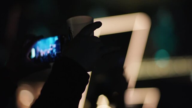 Fan raises hands above head in crowd at concert, wristband and arm visible, soft purple pink stage bokeh light fills entire background