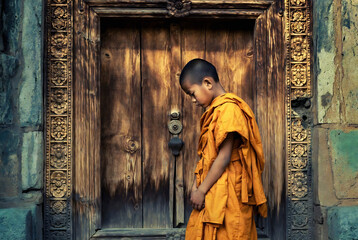 Obraz premium A young Buddhist monk stands before an ornate wooden door at Angkor Wat, Cambodia.